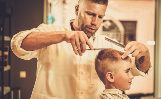 A man cutting another mans hair with scissors and comb.