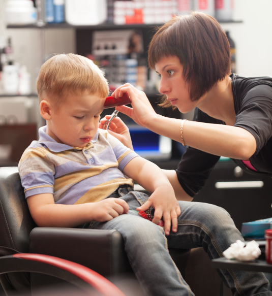 A woman is cutting the hair of a boy.