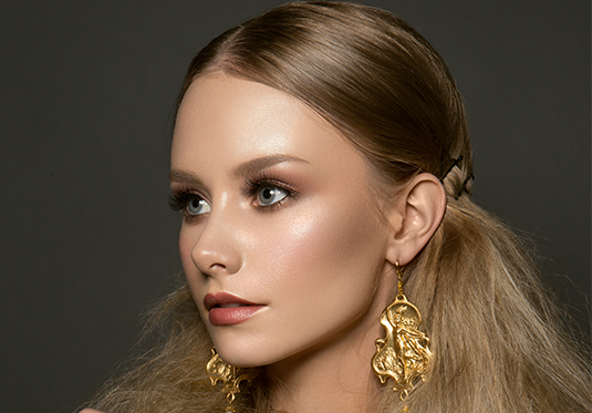 A woman with long blonde hair wearing gold earrings.