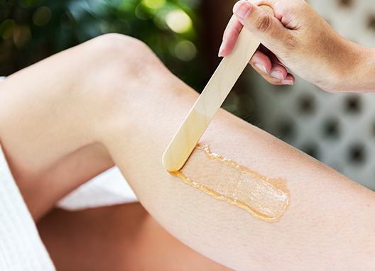 A person is waxing their leg with a wooden spatula.