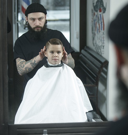 A man is cutting the hair of a young boy.