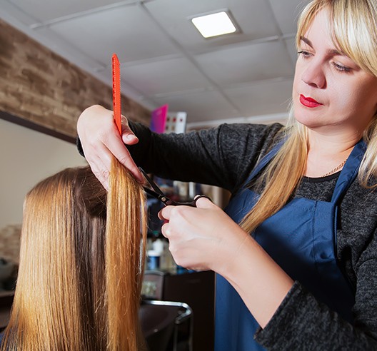 A woman cutting another person 's hair in a salon.