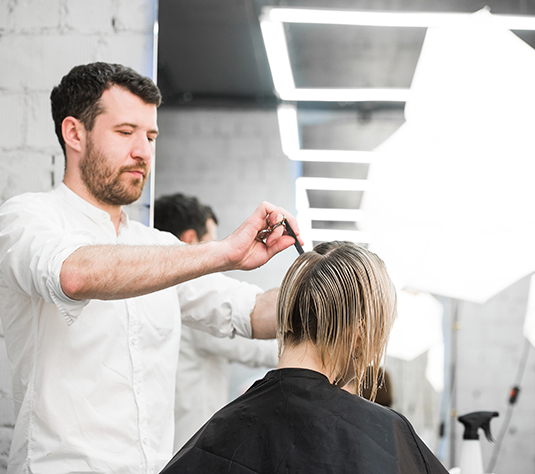 A man cutting another woman 's hair in a salon.