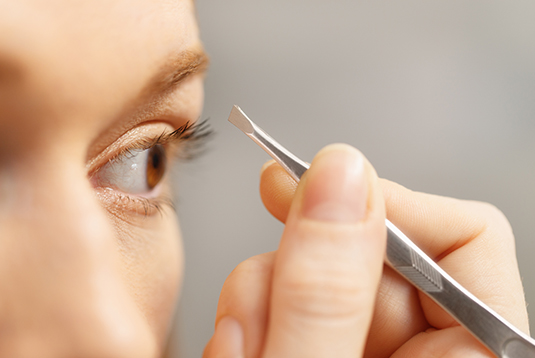 A person is using tweezers to remove makeup.