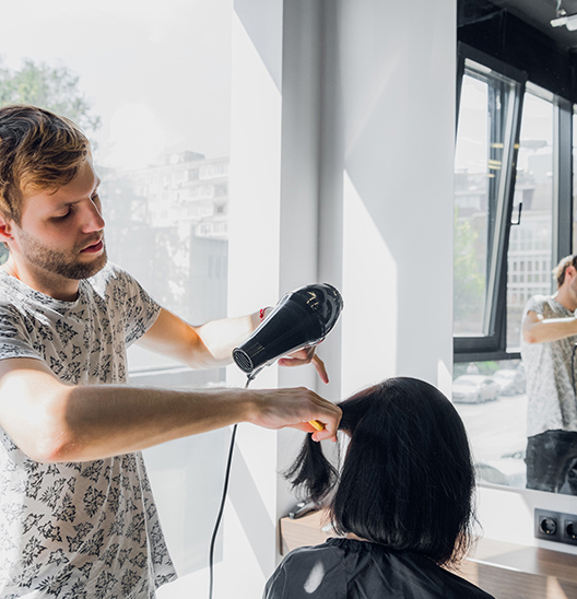 A man blow drying the hair of another woman.